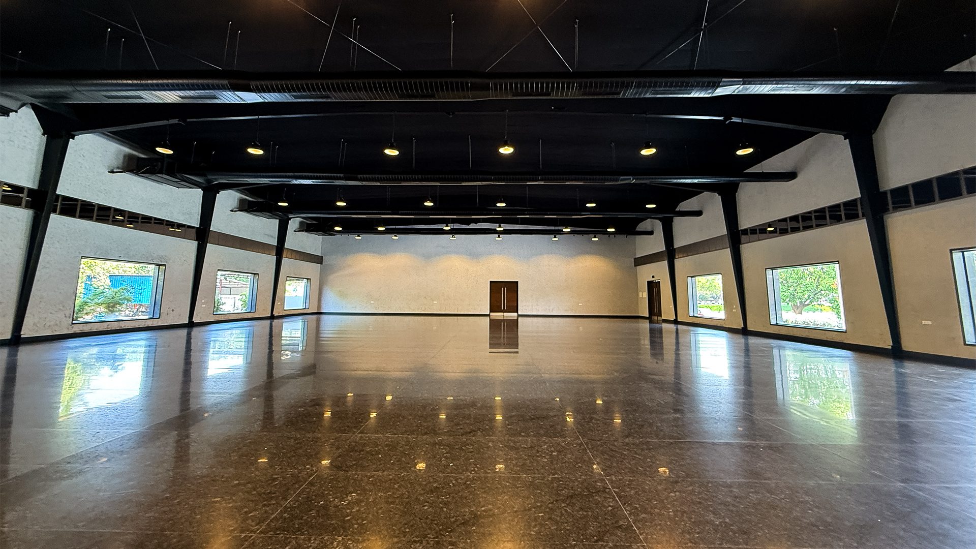 Ruby hall empty, showing black steel trusses, angled black columns, cream textured walls and window bays with greenery outside